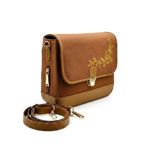 A brown denim crossbody bag by needlesay with a flap front, gold floral embroidery, a side zipper, and a detachable shoulder strap, displayed on a clean white background.