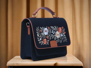 Needlesay Noir, black denim handbag with floral embroidery on a beige surface