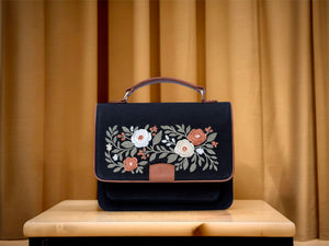 Needlesay Noir Black handbag with floral embroidery on a wooden table against a beige curtain