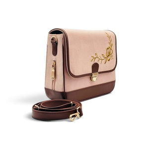 A rectangular needlesay botanica blush shoulder bag in light blush pink and dark brown with gold floral embroidery on the front flap, shown with a detachable brown shoulder strap on a white background.