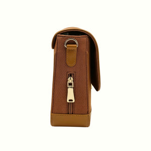 A brown denim shoulder bag from needlesay collection called botanica cocoa shown from the side, featuring a vertical zippered pocket with a gold-tone pull and a matching brown leather tab with a metal ring.